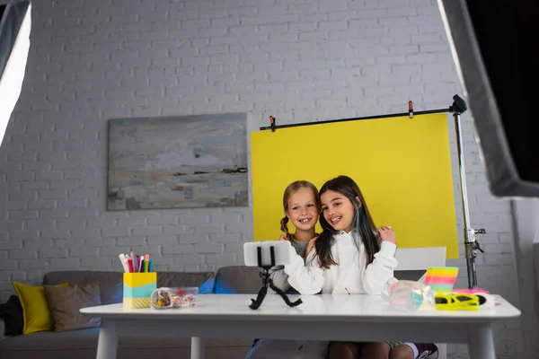 Cheerful video bloggers talking on yellow background at home near smartphone on phone holder — Stock Photo