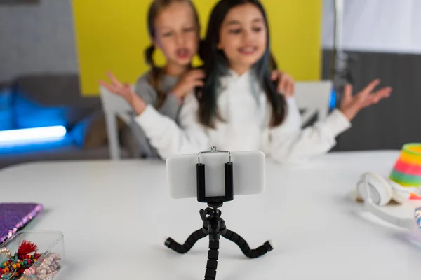 Selective focus of smartphone on phone holder near bloggers talking on blurred background — Stock Photo