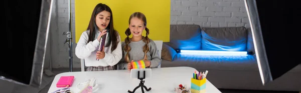 Chicas con portátil y espiral video blog grabación de juguetes en el teléfono inteligente en casa, pancarta - foto de stock