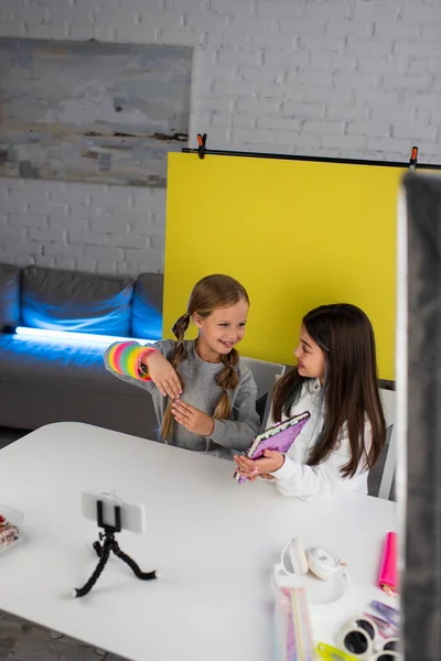 Smiling bloggers with notebook and spiral toy talking in front of smartphone on holder — Stock Photo