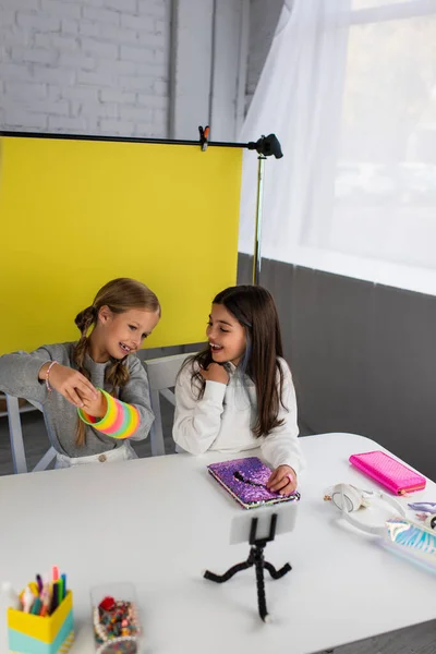 Video blogger sosteniendo un juguete en espiral cerca de un amigo sonriente y titular con teléfono móvil en primer plano borroso - foto de stock