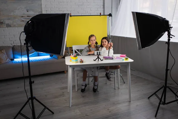 Preteen girls talking during video blog on yellow background near lamps at home — Stock Photo