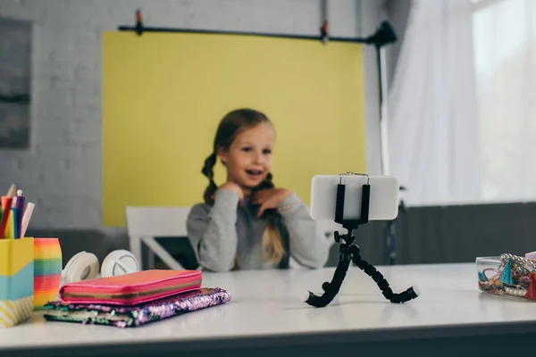 Preteen Blogger spricht in der Nähe Smartphone auf Halter und verschiedene Accessoires auf Tisch auf gelbem Hintergrund zu Hause — Stockfoto