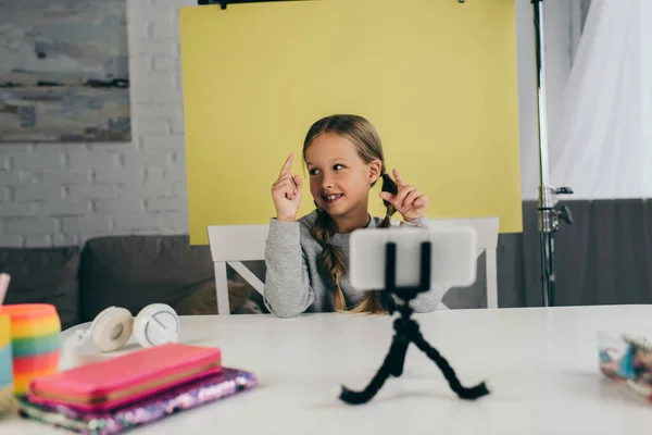 Усміхнена дівчина вказує пальцями під час запису відео блогу на смартфон вдома на жовтому фоні — стокове фото