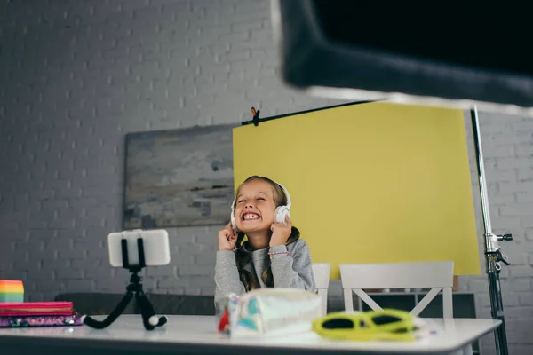 Blogueur excité avec les yeux fermés écouter de la musique dans les écouteurs sans fil près de smartphone flou sur le titulaire du téléphone — Photo de stock