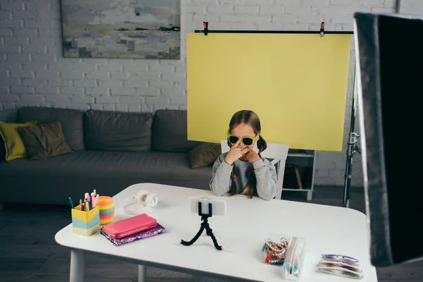 Alegre chica en gafas de sol grabación video blog cerca de diferentes accesorios sobre fondo amarillo en casa - foto de stock