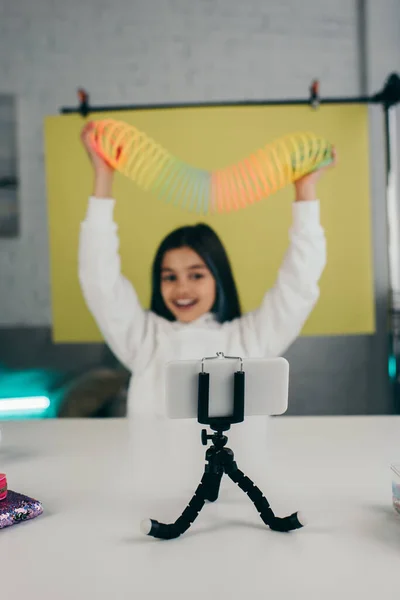 Blurred video blogger holding spiral toy in raised hands near mobile phone on holder — Stock Photo