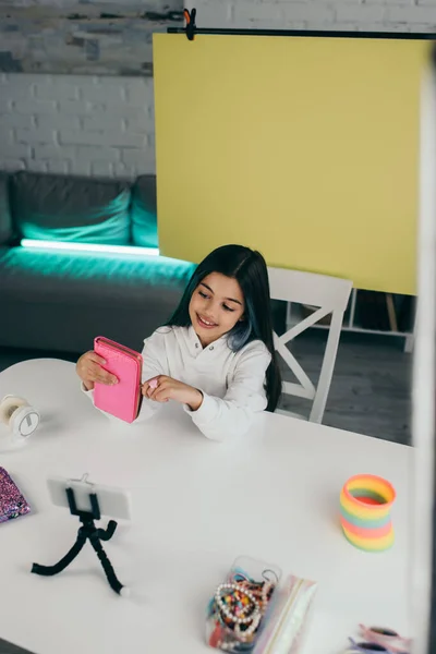 Glückliche Brünette, die ein Mäppchen hält, während sie zu Hause Videoblog auf gelbem Hintergrund aufzeichnet — Stockfoto