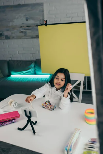 Brünettes Mädchen mit Perlenarmband in der Nähe von Smartphone auf Halter und Mäppchen mit drahtlosen Kopfhörern — Stockfoto