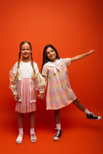 Smiling girl with pigtails holding hands with brunette friend posing with outstretched hand on orange background — Stock Photo