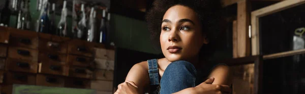 Young and dreamy african american woman sitting in art workshop and looking away, banner — Stock Photo