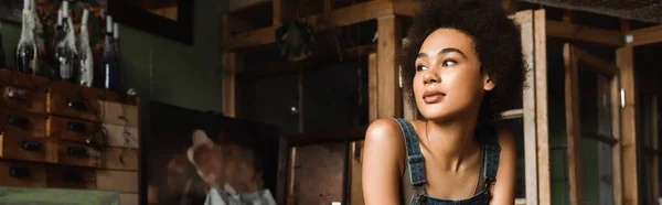 Giovane e sognante donna afro-americana che distoglie lo sguardo nel laboratorio d'arte, banner — Foto stock