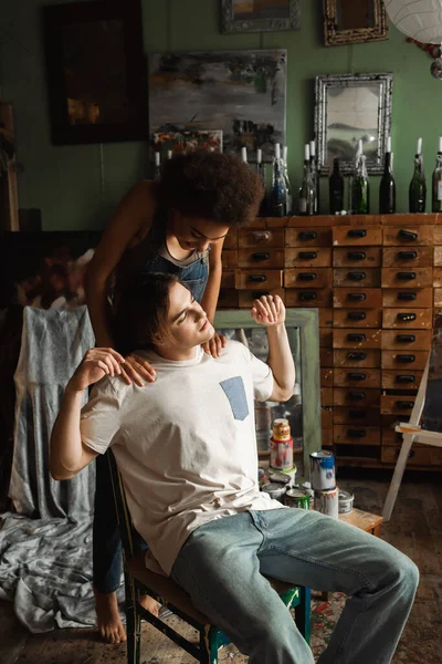 African american woman touching shoulders of young artist sitting with closed eyes in art studio — Stock Photo