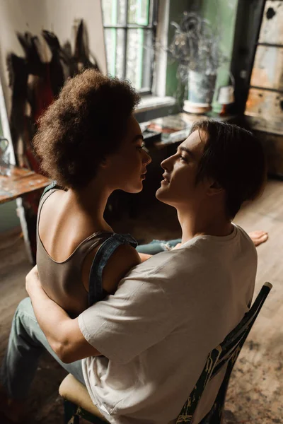 Jovem casal interracial abraçando e olhando uns para os outros no estúdio de arte — Fotografia de Stock