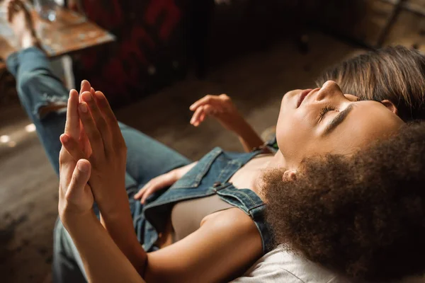 Vista aérea de la seductora mujer afroamericana con los ojos cerrados uniendo las manos con su novio en el taller - foto de stock