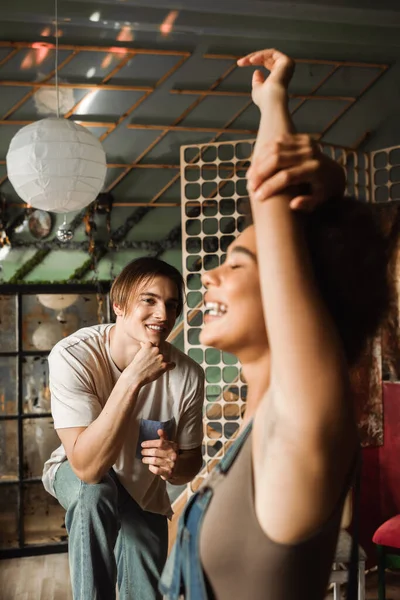 Artista sorrindo olhando para feliz afro-americana namorada posando com a mão levantada em primeiro plano borrado — Fotografia de Stock