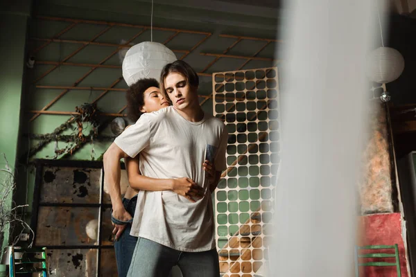 Sensual african american woman hugging young artist in workshop on blurred foreground — Stock Photo