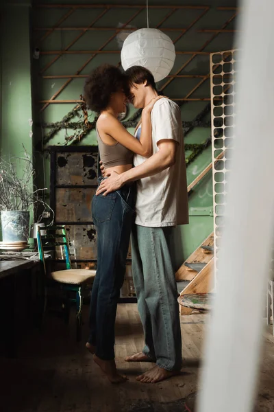 Side view of barefoot interracial couple embracing face to face in art studio on blurred foreground — Stock Photo