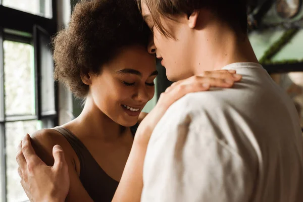 Sensual mujer afroamericana sonriendo cerca de joven artista en taller de arte — Stock Photo