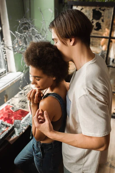 Aus der Vogelperspektive: Mann umarmt junge und hübsche afrikanisch-amerikanische Freundin in Werkstatt — Stockfoto