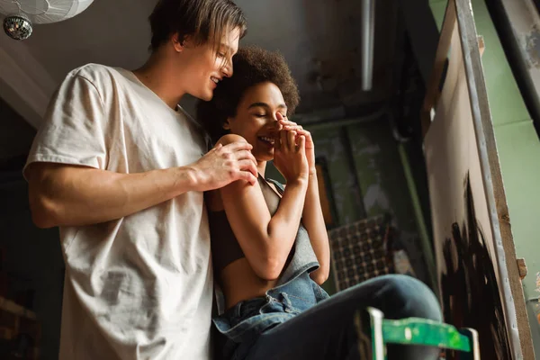 Cheerful african american woman laughing near young boyfriend in art workshop — Stock Photo