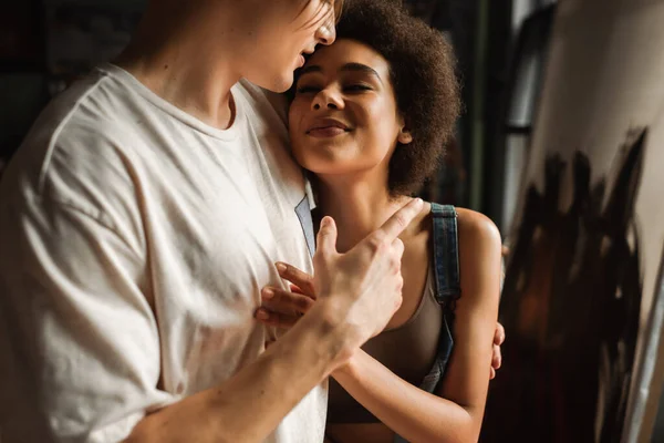 Brünette afrikanisch-amerikanische Frau lächelt in der Nähe Künstler umarmt sie in der Werkstatt — Stockfoto