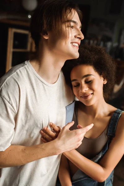 Young african american woman with closed eyes leaning on smiling artist in workshop — Stock Photo