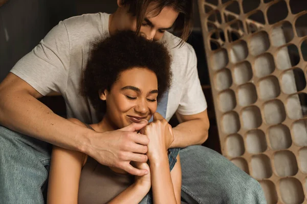 Junge Künstlerin umarmt glückliche Afroamerikanerin lächelnd mit geschlossenen Augen in Werkstatt — Stockfoto