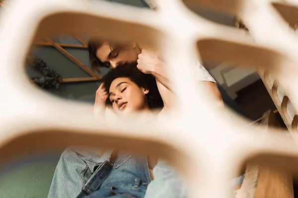 Low angle view of sensual interracial couple with closed eyes holding hands near blurred decorative lattice — Stock Photo