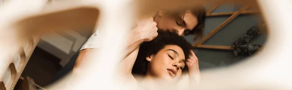 Low angle view of passionate interracial couple with closed eyes holding hands on blurred foreground, banner — Stock Photo