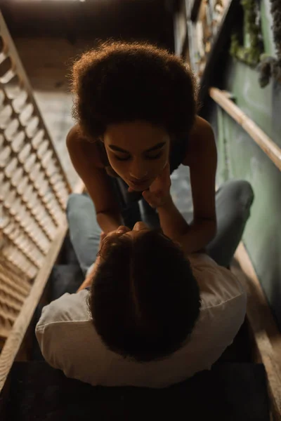 Overhead view of seductive african american woman near young man sitting on stairs in workshop — Stock Photo