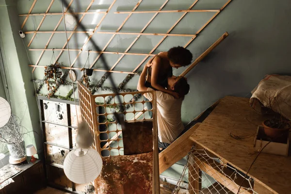 Sexy interracial couple embracing on stairs near decorative grid in art workshop — Stock Photo