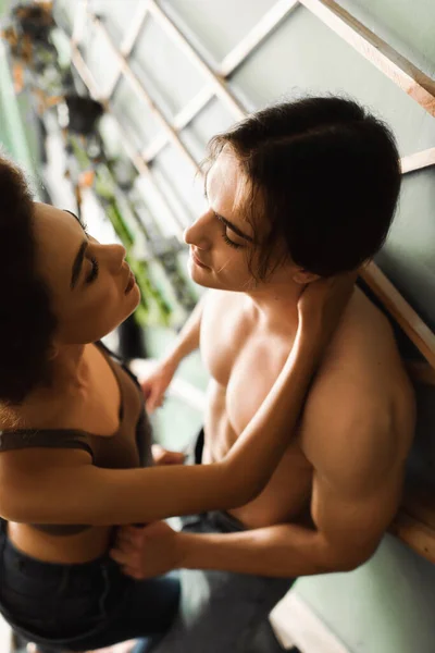 Hochwinkelaufnahme eines hemdlosen muskulösen Mannes und einer sexy afrikanisch-amerikanischen Frau, die sich in einem Kunstworkshop umarmen — Stockfoto