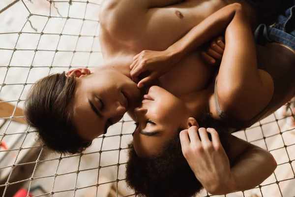 Top view of shirtless man and seductive african american woman touching each other with closed eyes in mesh hammock — Stock Photo