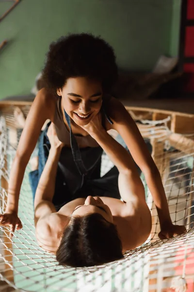 Young and sexy african american woman smiling over shirtless man in mesh hammock — Stock Photo