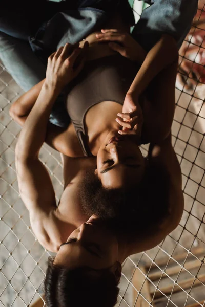 Top view of young shirtless man embracing african american woman in top on mesh hammock in art studio — Stock Photo