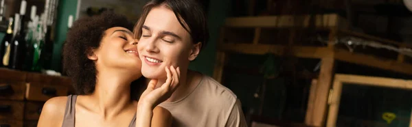 Seductive african american woman kissing smiling boyfriend with closed eyes in art workshop, banner — Stock Photo