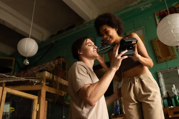 Vista de ángulo bajo de sonrientes artistas interracial sosteniendo la cámara vintage en el estudio de arte — Stock Photo