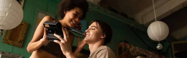 Low angle view of smiling multiethnic couple holding vintage camera in workshop, banner — Stock Photo