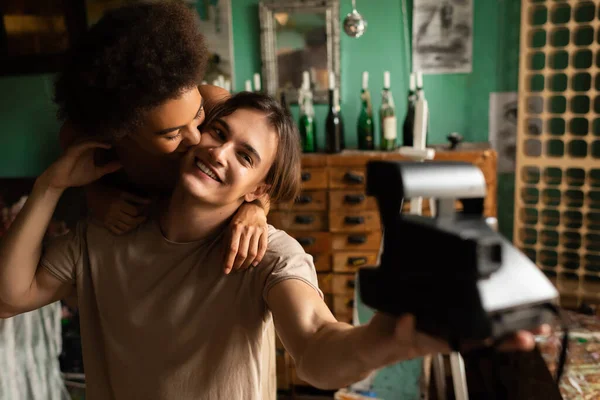 Sensual african american woman embracing smiling boyfriend taking selfie on blurred vintage camera — Stock Photo