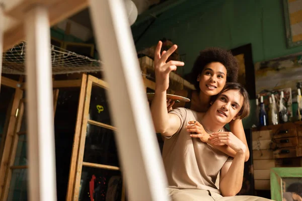 Afro-américaine femme près copain pointant vers chevalet sur flou premier plan — Photo de stock