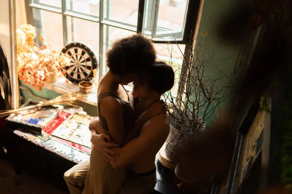 High angle view of multiethnic couple hugging near window and dried plants in art studio — Stock Photo