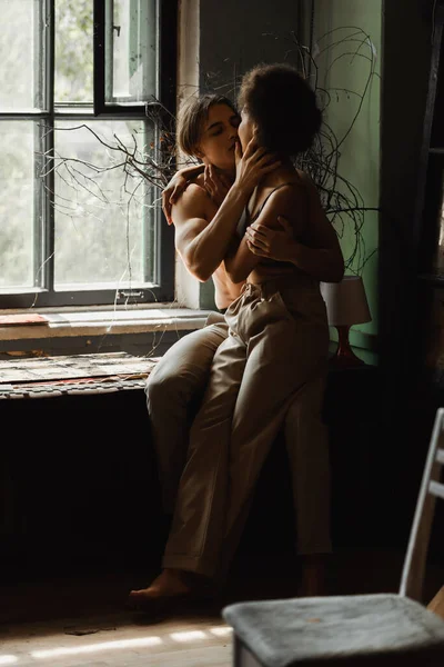 Passionate interracial couple kissing and embracing near window in workshop — Stock Photo