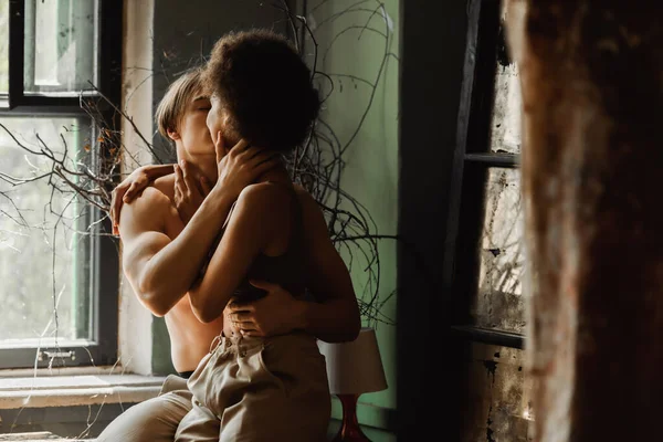 Passionate interracial couple embracing and kissing near dried plants and window in art workshop — Stock Photo