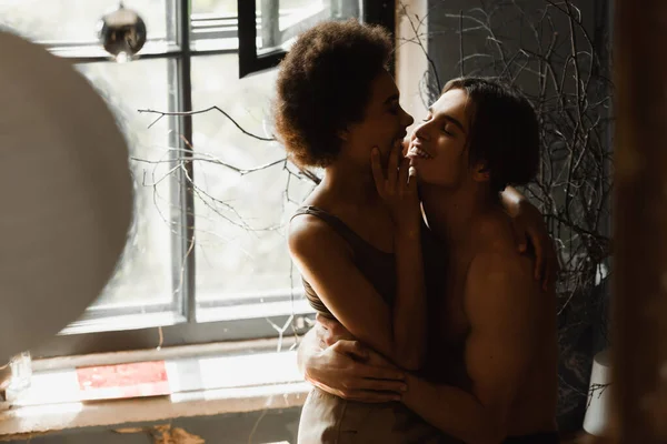 Smiling shirtless and muscular man embracing african american girlfriend in workshop — Stock Photo