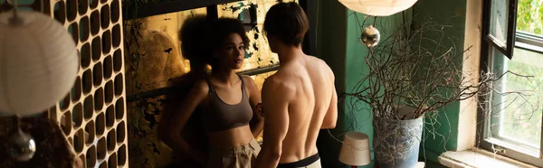 Соблазнительная африканская американка, стоящая рядом с поцарапанным винтажным стеклом перед мускулистым мужчиной без рубашки, баннер — стоковое фото
