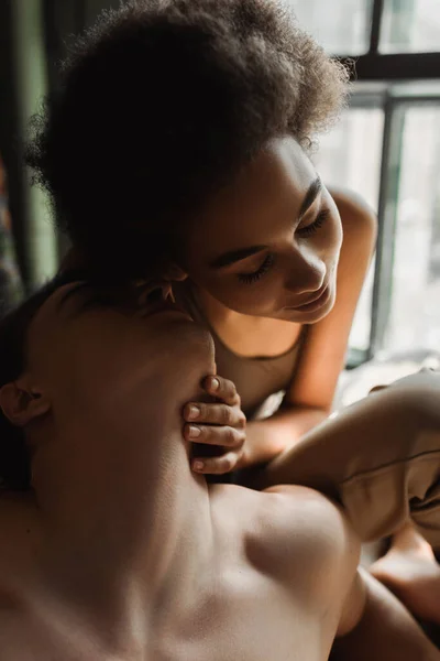 Séduisante femme afro-américaine aux yeux fermés près de l'homme torse nu dans un atelier d'art — Photo de stock