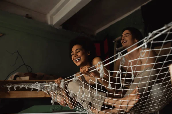 Excited african american woman laughing in hammock near smiling shirtless boyfriend — Stock Photo
