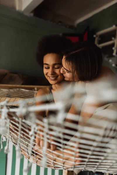 Young artist kissing happy and pretty african american woman while sitting in hammock — Stock Photo