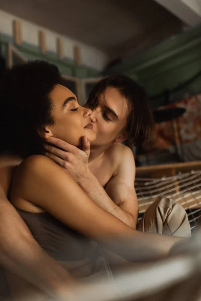 Young shirtless man kissing pleased african american woman in mesh hammock — Stock Photo